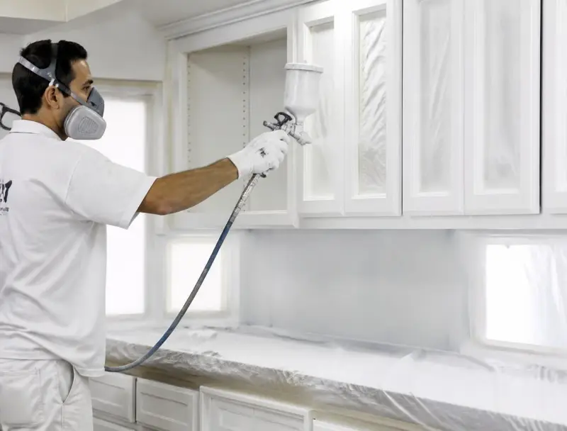 Painter spraying kitchen cabinets a fresh white finish